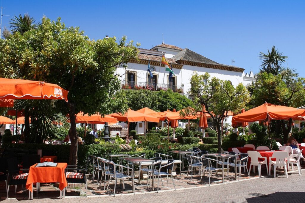 Café terraces with orange parasols under trees in Plaza de los Naranjos, Marbella old town